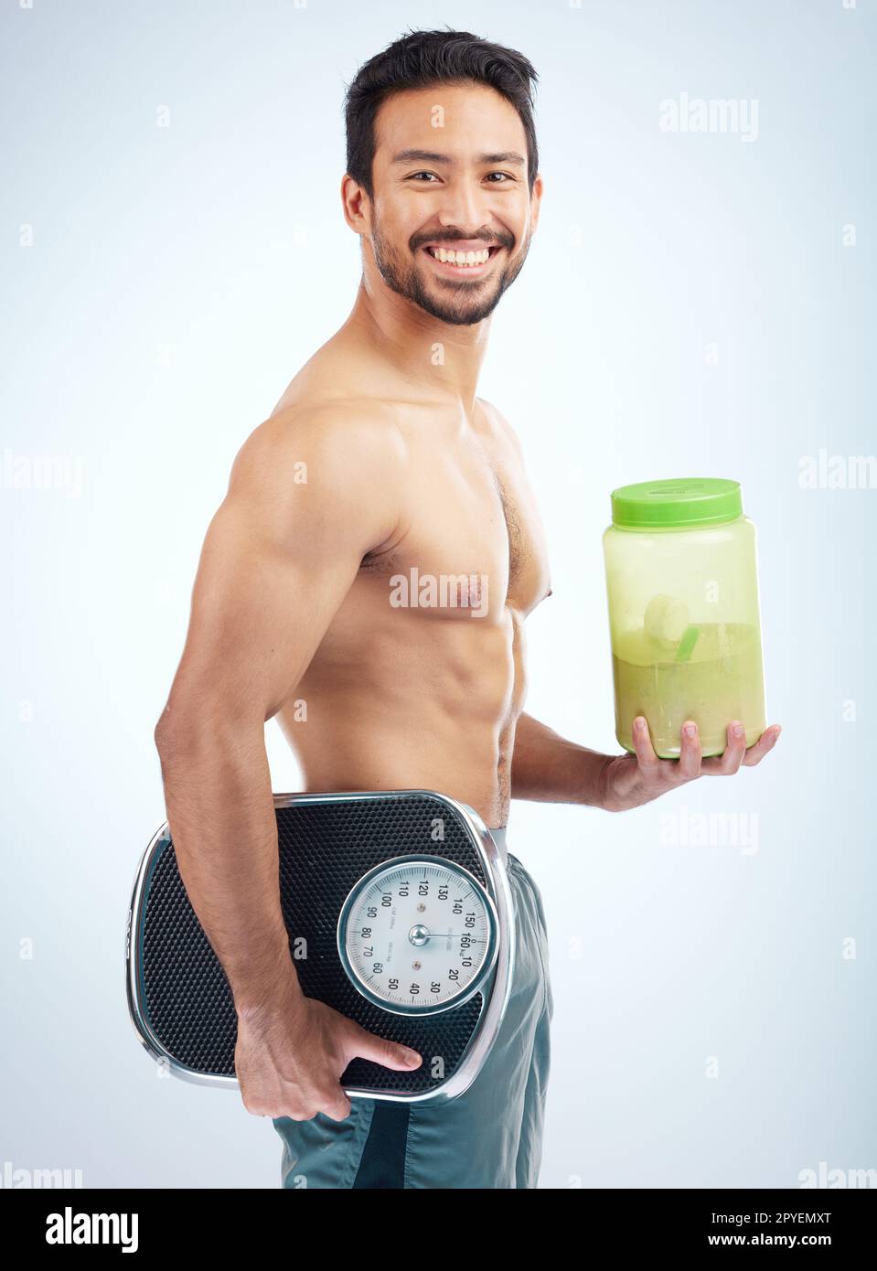 Uomo, dieta o polvere di proteine del corpo su sfondo blu studio in perdita di peso, bodybuilding o crescita muscolare giapponese. Ritratto, sorriso o atleta felice con bilancia o supplemento benessere sanitario Foto Stock