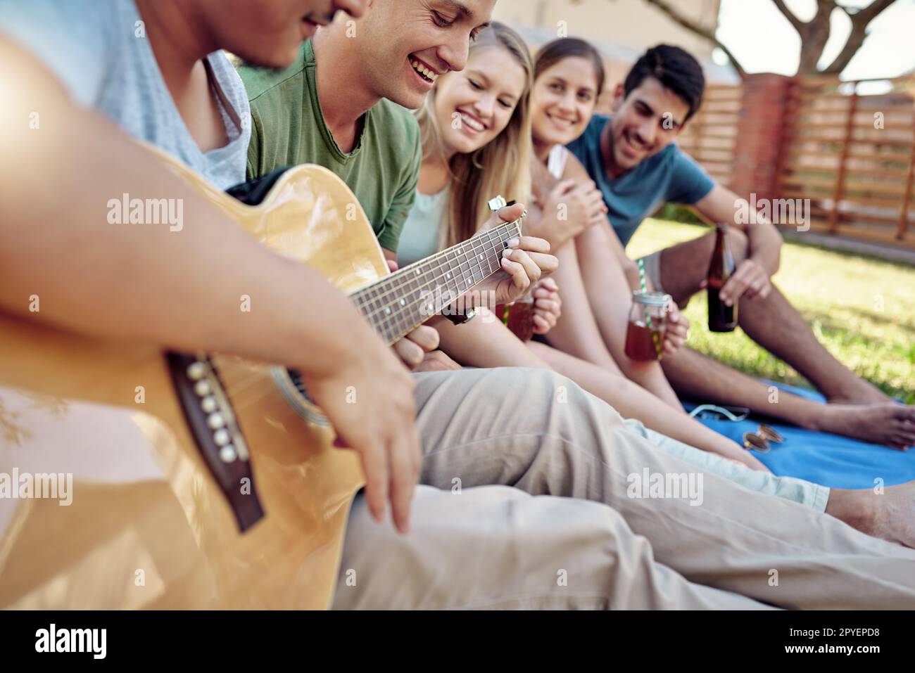 Riproduzione di una canzone. un giovane che suona la chitarra mentre sorsegga qualche drink con i suoi amici fuori nel sole estivo. Foto Stock