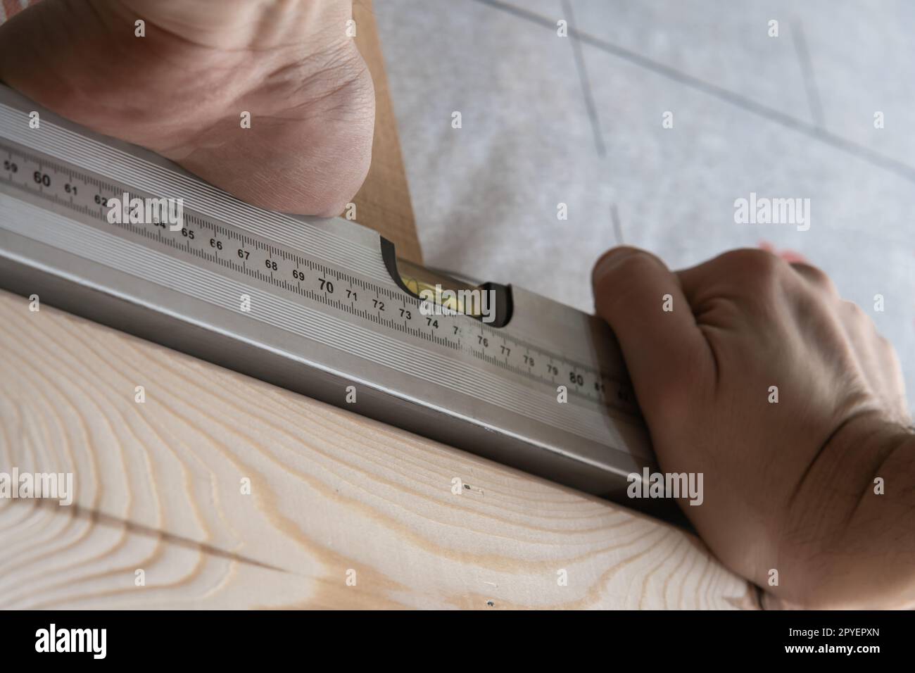 Le mani di un lavoratore maschio ritagliato tengono il livello del passaggio d'acqua per la costruzione di strutture in legno. Ristrutturazione e riparazione di case Foto Stock
