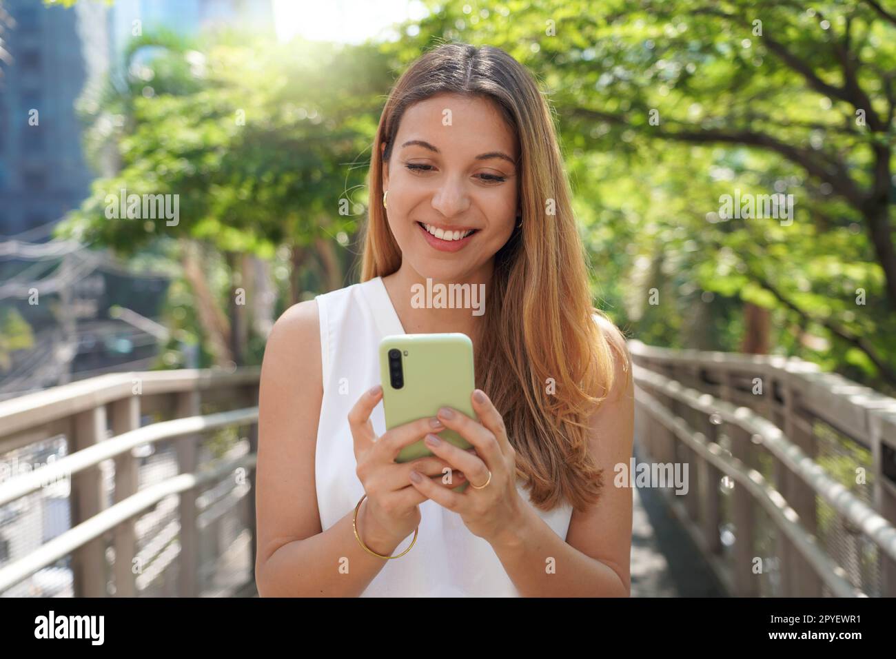 Giovane bella donna che usa lo smartphone in una città. Ragazza elegante e sorridente che invia messaggi sul cellulare all'aperto. Stile di vita moderno, connessione, concetto di business informale. Foto Stock