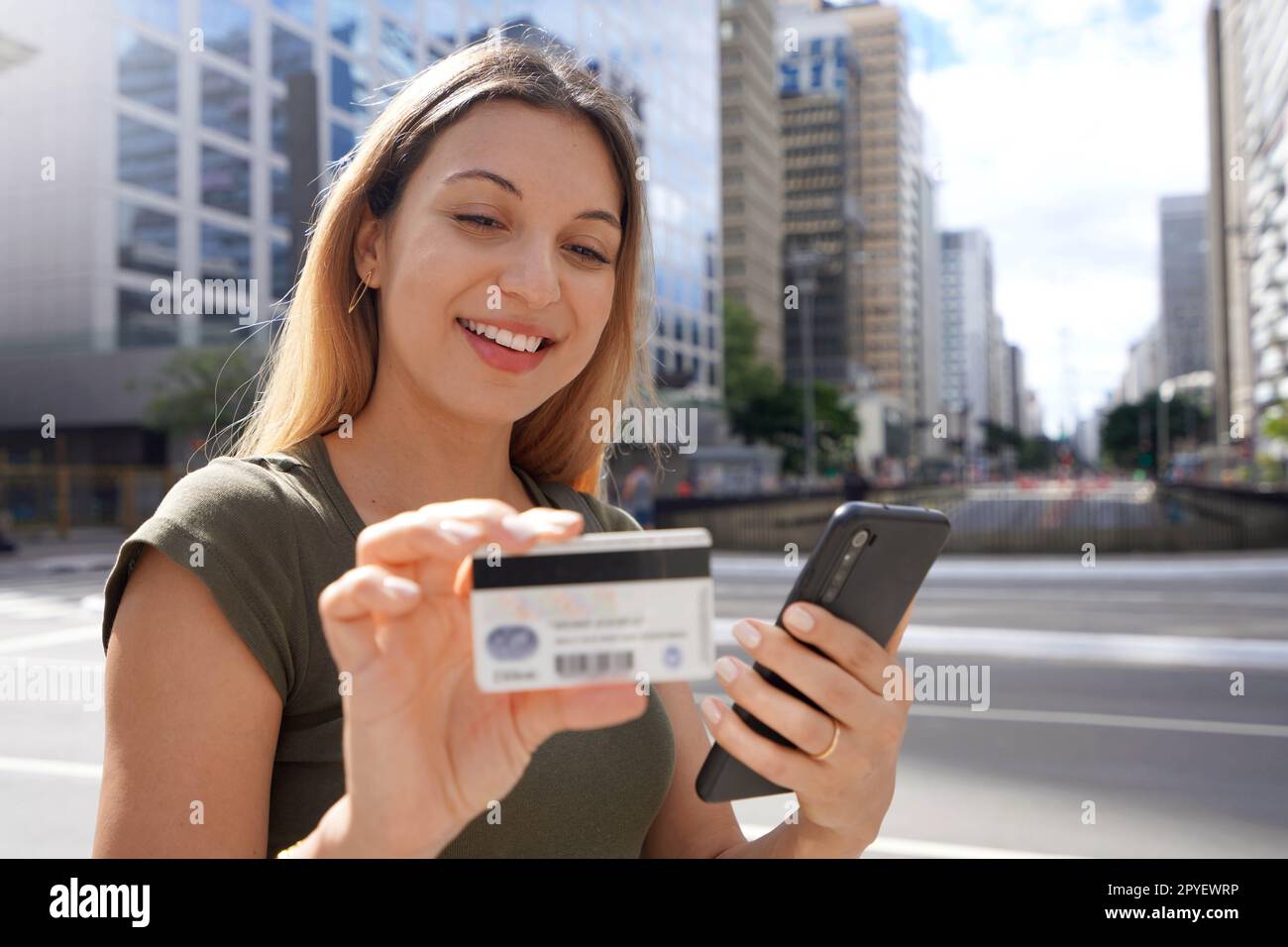 Bella giovane donna che guarda il suo numero di carta di credito utilizzando il suo smartphone per lo shopping online nel distretto finanziario Foto Stock