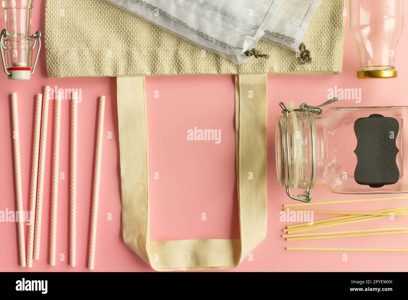 Borse in tessuto di cotone, bottiglie di vetro, cannucce di carta e bastoncini di legno su sfondo rosa. Vista dall'alto. Copia spazio. Foto Stock