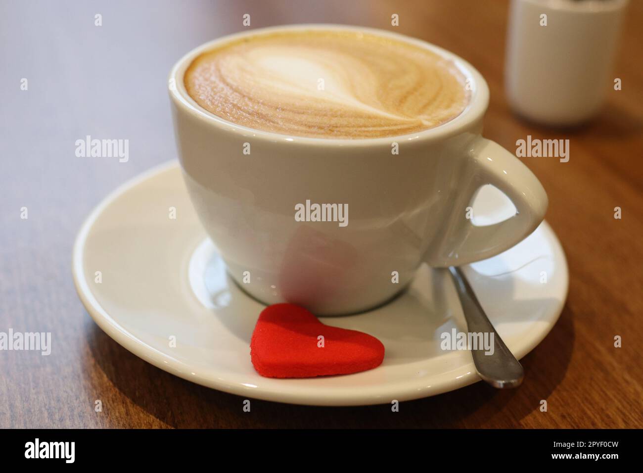 Una tazza di caffè latte in ceramica bianca si trova su un piattino abbinato, con un cucchiaio d'argento Foto Stock
