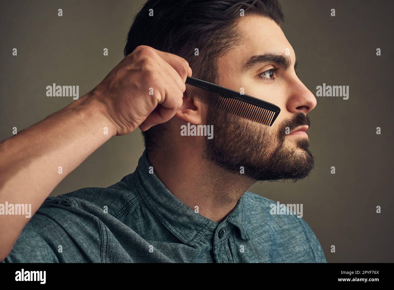 I capelli facciali hanno bisogno della vostra attenzione. un bel giovane che pettina la barba su uno sfondo grigio. Foto Stock
