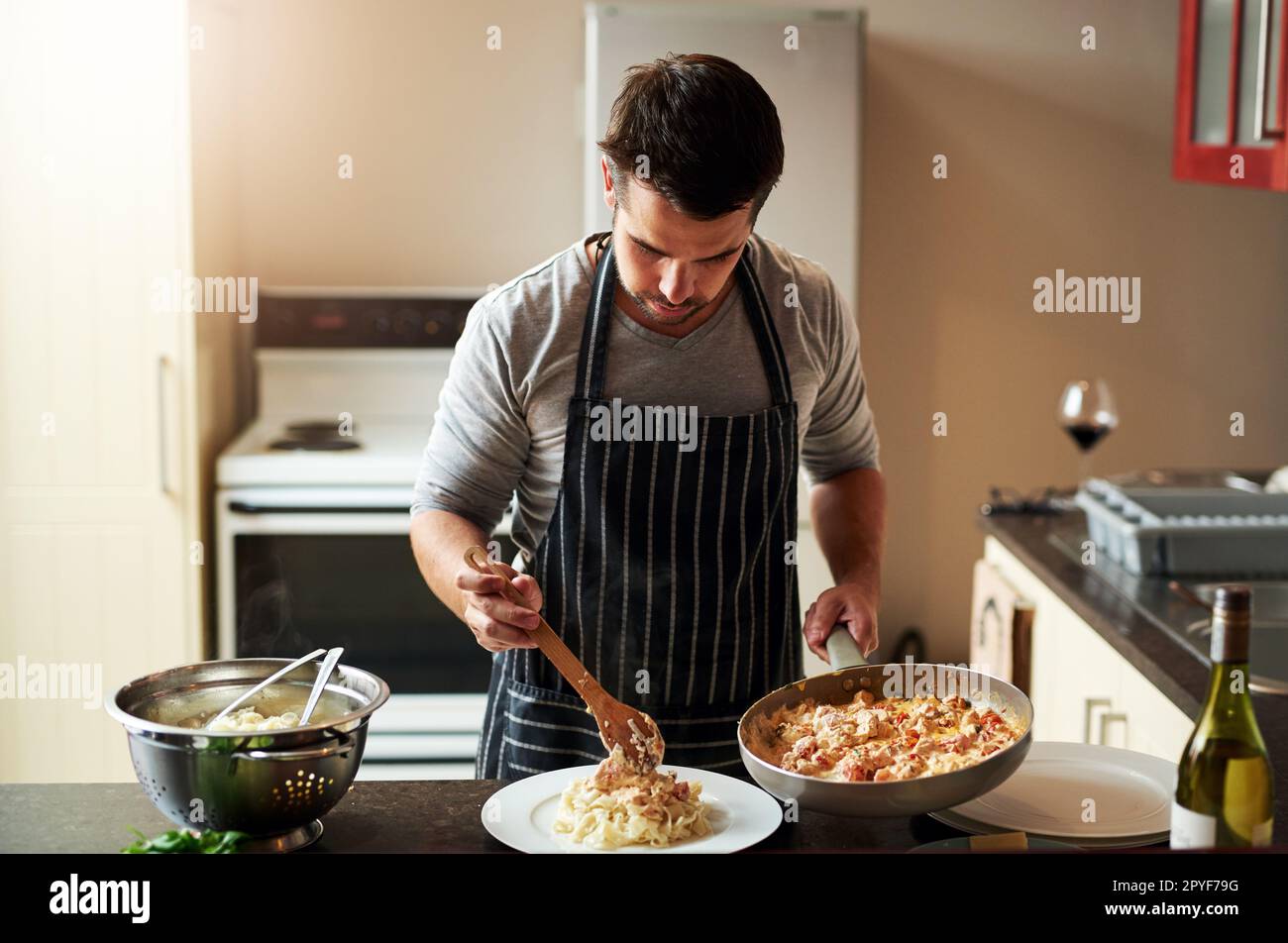 Godendo il processo di cottura, cominciando a finire. Un bel giovane che sta mangiando cibo in cucina a casa. Foto Stock