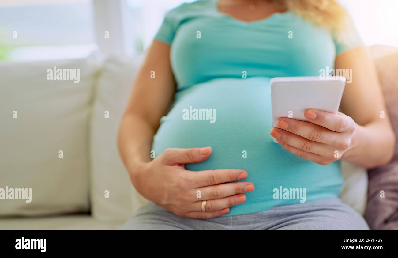 Inviare un conto alla rovescia per i suoi vicini. Primo piano di una donna incinta che SMS sul suo cellulare a casa. Foto Stock