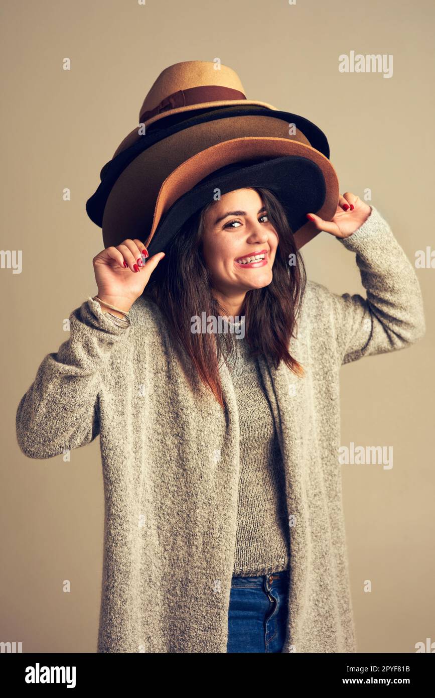 Devo avere il cappello perfetto prima di uscire. Studio shot di una giovane donna che indossa un mucchio di cappelli su uno sfondo marrone. Foto Stock