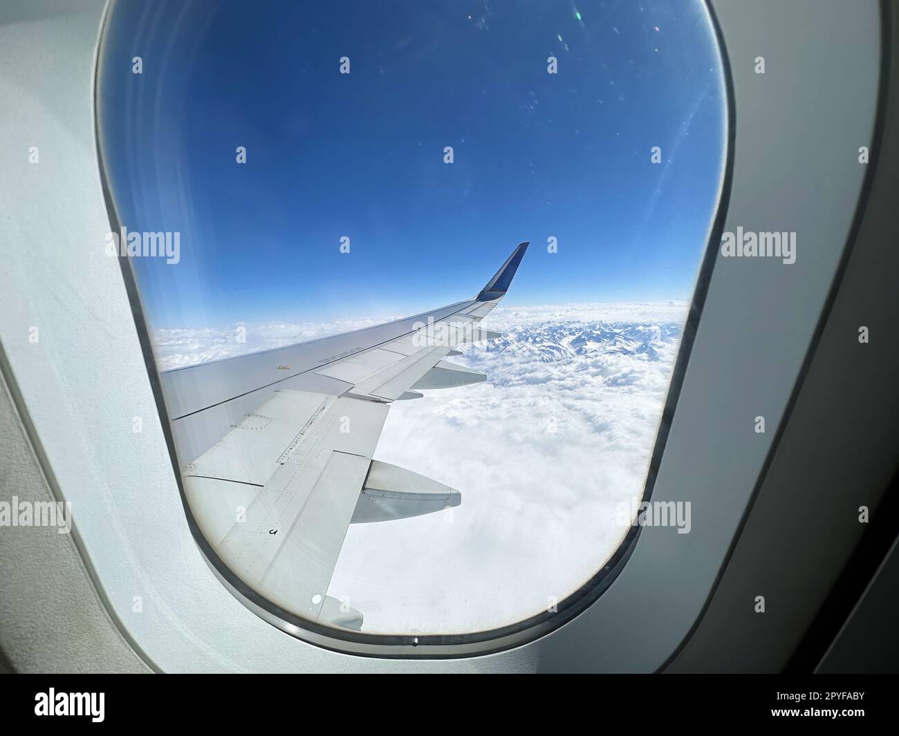 Vista dell'ala dell'aeromobile dalla finestra all'interno dell'aereo. Sorvola la catena montuosa innevata Foto Stock