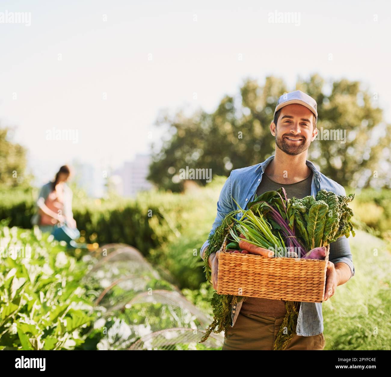 Per una cena fresca. Ritratto di un giovane contadino felice che raccoglie erbe e verdure in un cestino della sua fattoria. Foto Stock