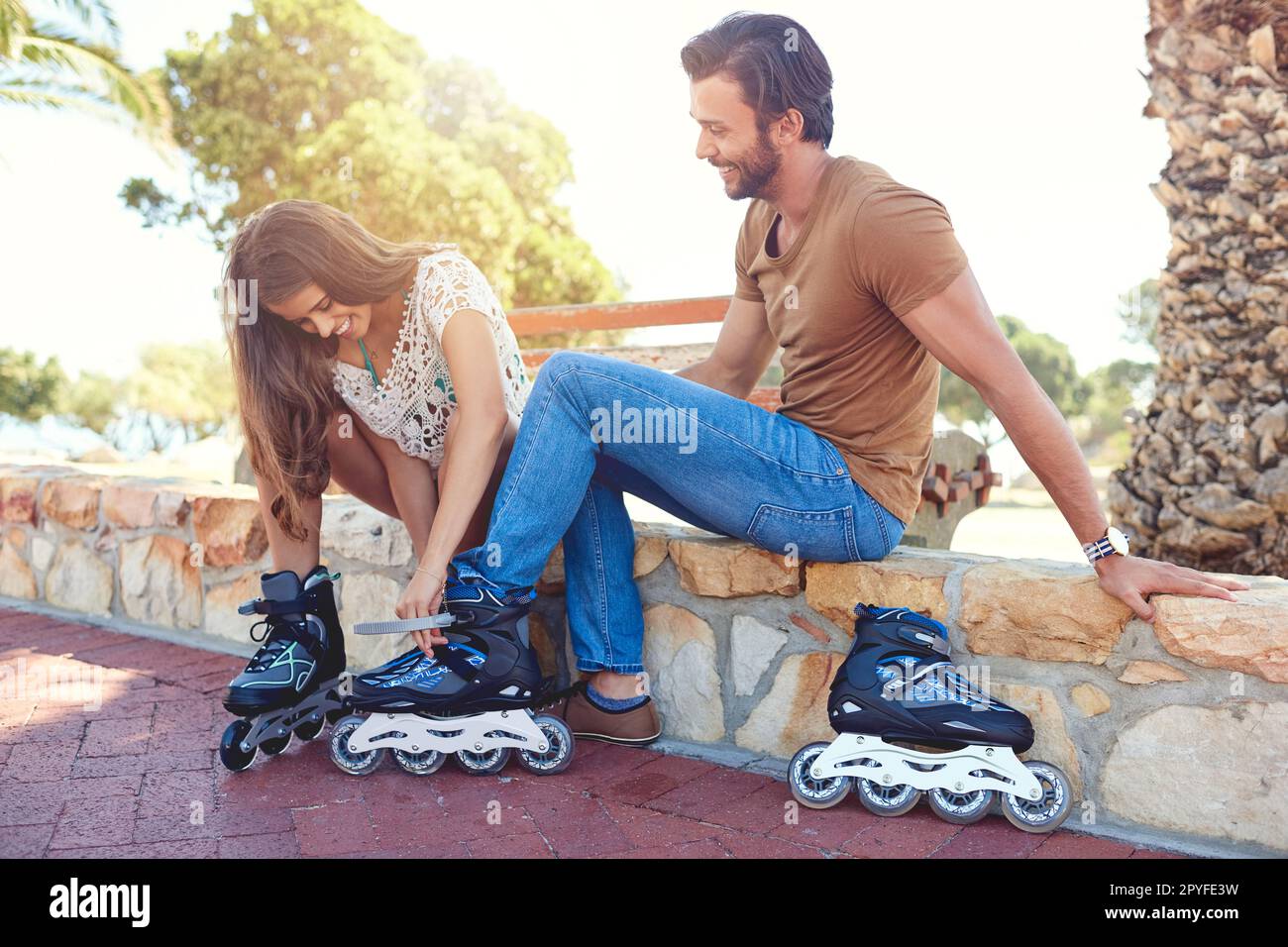 Ne avrai la possibilità. una donna che aiuta il suo ragazzo a mettere su rollerblade in un parco. Foto Stock