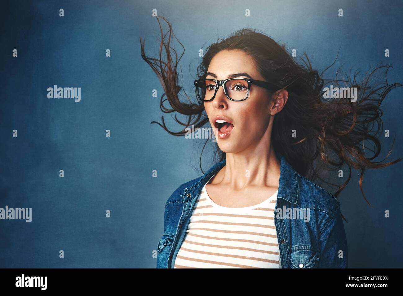 WOah che ha acceso l'aria condizionata. Studio shot di una giovane donna con aria soffiata in faccia su uno sfondo blu. Foto Stock