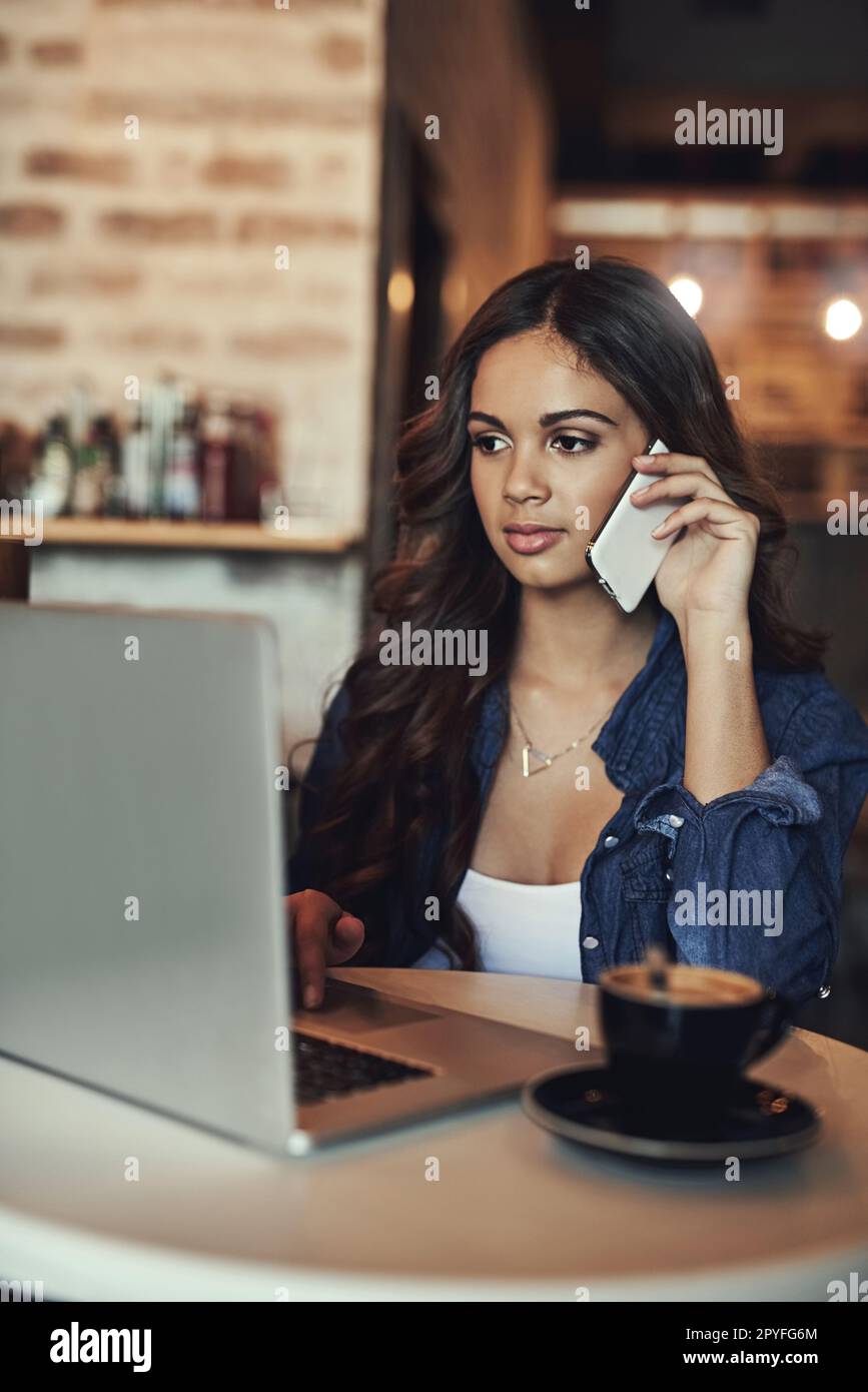 La tecnologia wireless le consente di lavorare ovunque. una giovane donna che risponde al suo cellulare mentre usa il suo portatile in una caffetteria. Foto Stock