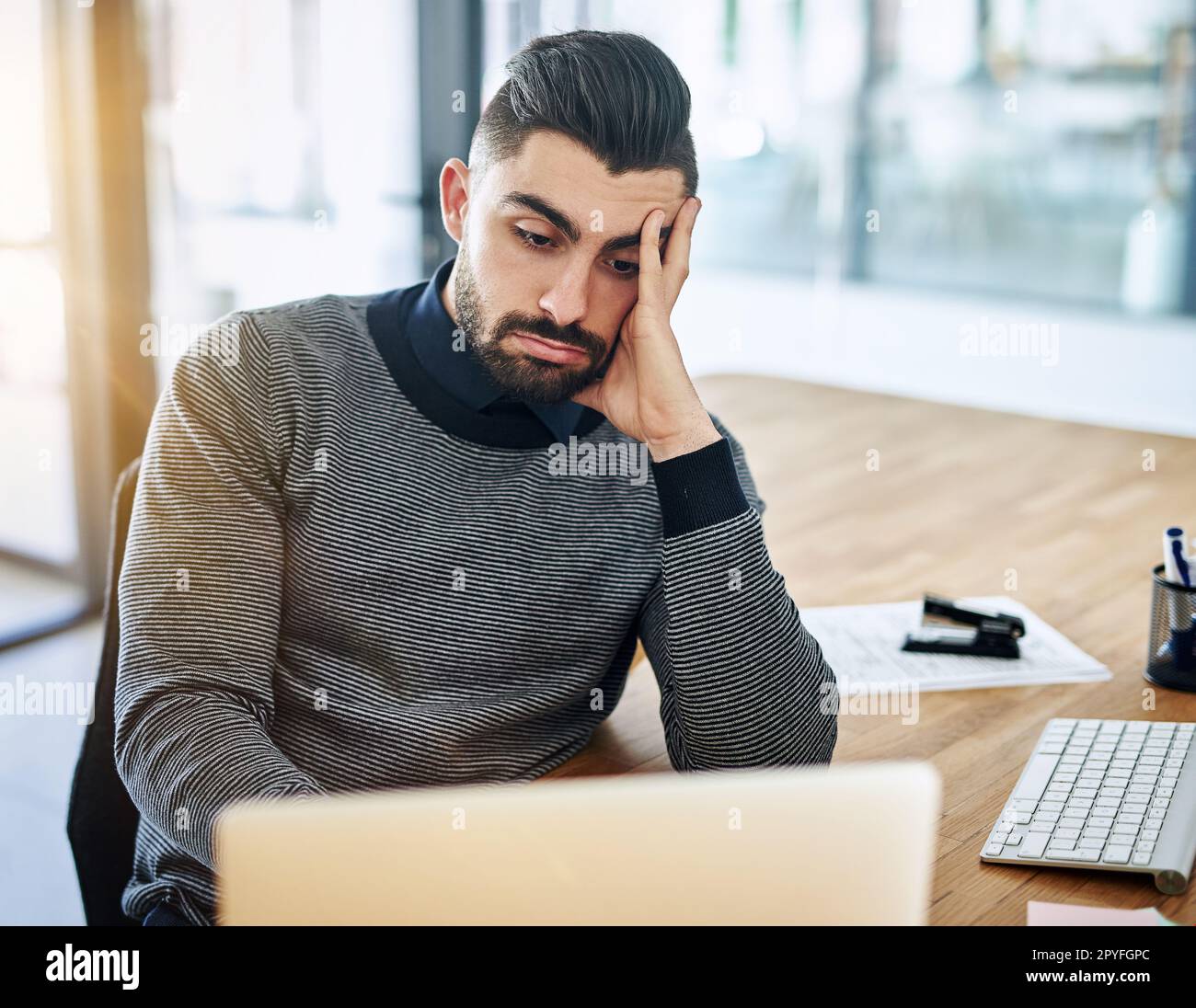 Potrebbe questo lavoro ottenere più noioso... un giovane designer che guarda annoiato mentre lavora in un ufficio. Foto Stock