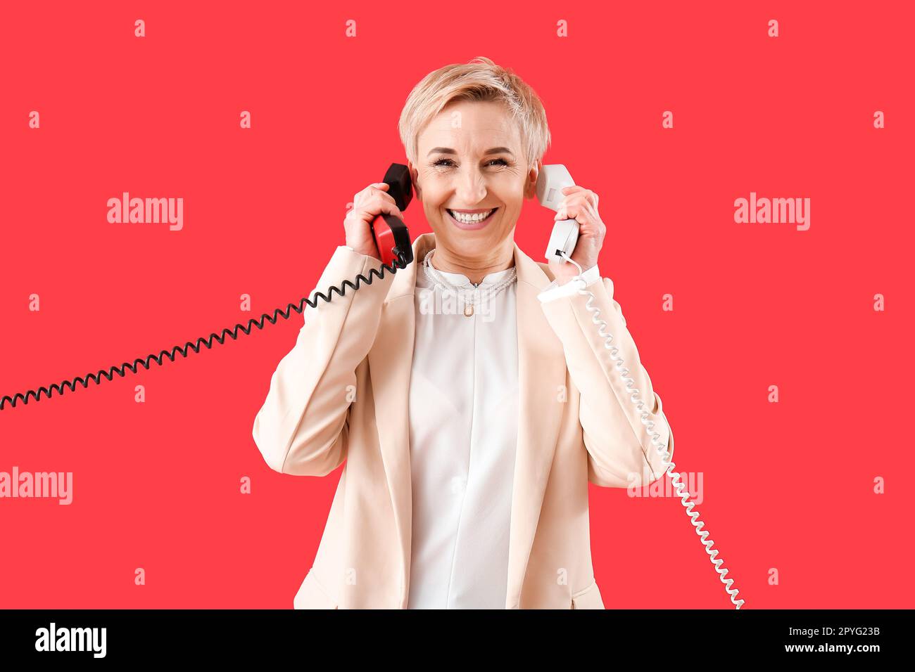 Donna matura con due ricevitori telefonici su sfondo rosso Foto Stock