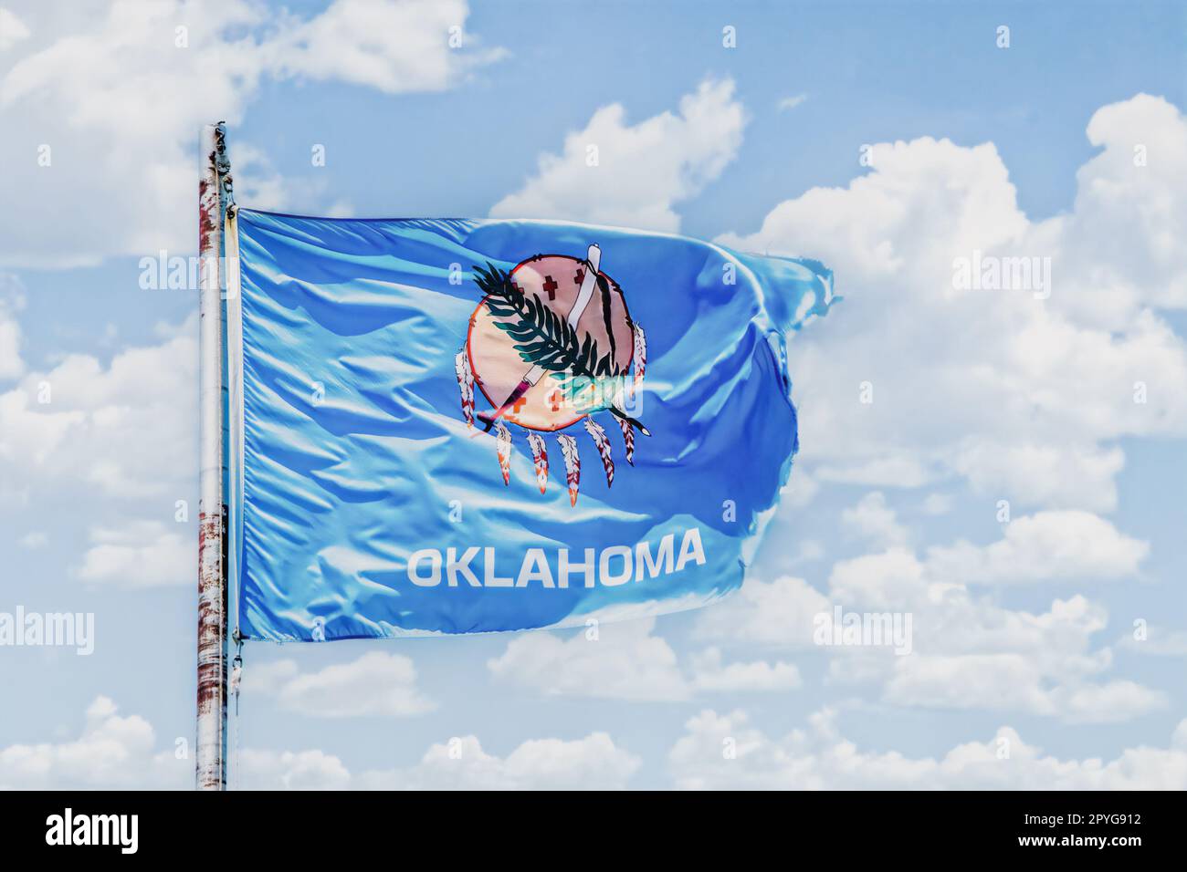 Bandiera dell'Oklahoma che vola in cielo nuvoloso ondeggiante su un flagpole arrugginito - stato degli Stati Uniti Foto Stock