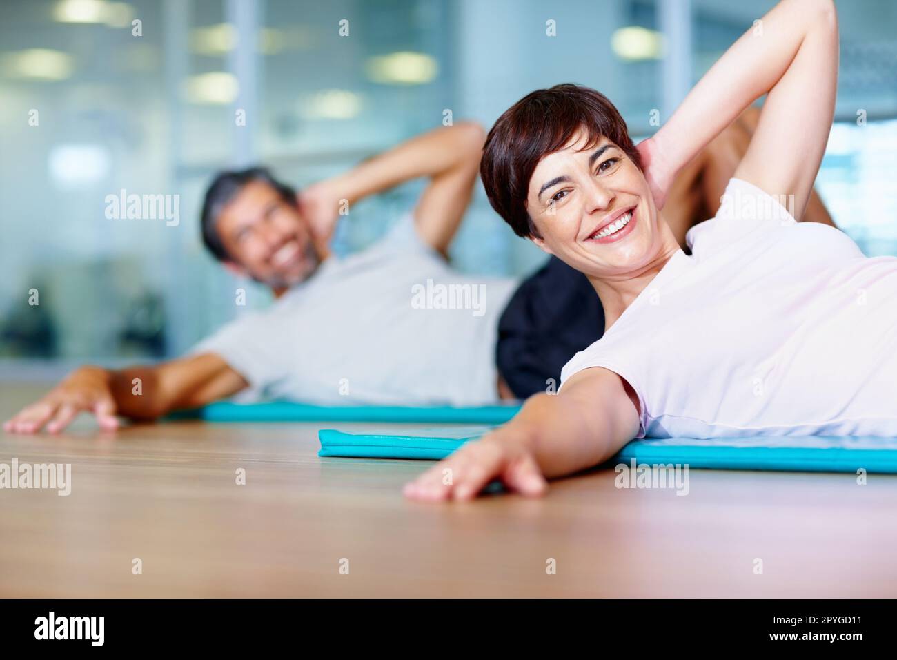 Donna che si esercita nel centro fitness. Bella donna che si esercita sul tappetino yoga con l'uomo sullo sfondo. Foto Stock