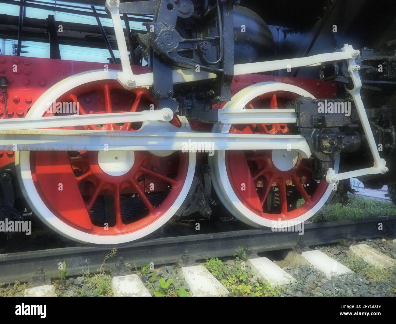 Ravvicinata delle ruote vintage di una locomotiva o di un treno. Ruote in metallo pesante grandi rosse con meccanismi di guida pistone. Locomotiva del XIX - XX secolo con motore a vapore. Messa a fuoco morbida sfocata Foto Stock