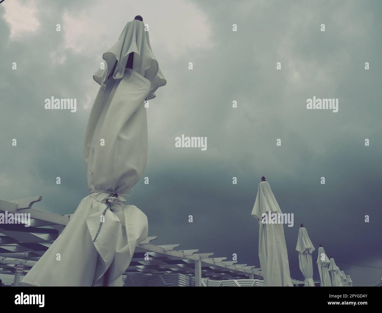 Lettini e ombrelloni bagnati sulla spiaggia di mare durante la forte pioggia. Ombrellone arrotolato sulla spiaggia contro il cielo nuvoloso scuro. Invasione di un tifone, ciclone o tempesta sul mare o sull'oceano Foto Stock