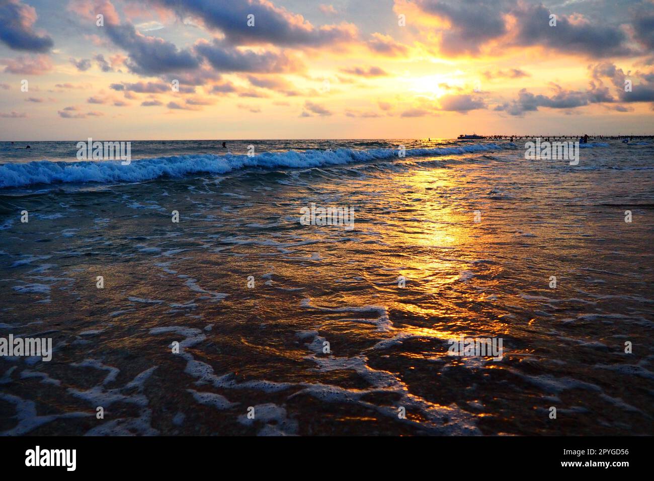 Onde e tramonti sul mare. Bel tramonto. Le onde schiumose si infrangono sulla spiaggia sabbiosa. Vityazevo, Anapa, Mar Nero. Mecca turistica, centro benessere. Cielo serale. I raggi si riflettono sull'acqua Foto Stock
