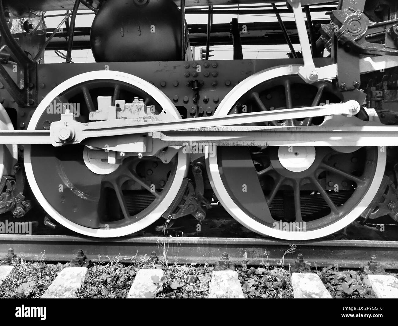 Treno retrò a due ruote. Traverse e rotaie, meccanismi, pistoni e guide. Locomotiva del XIX secolo all'inizio del XX secolo con motore a vapore. Stile vintage. Foto in bianco e nero. Bella carta. Foto Stock