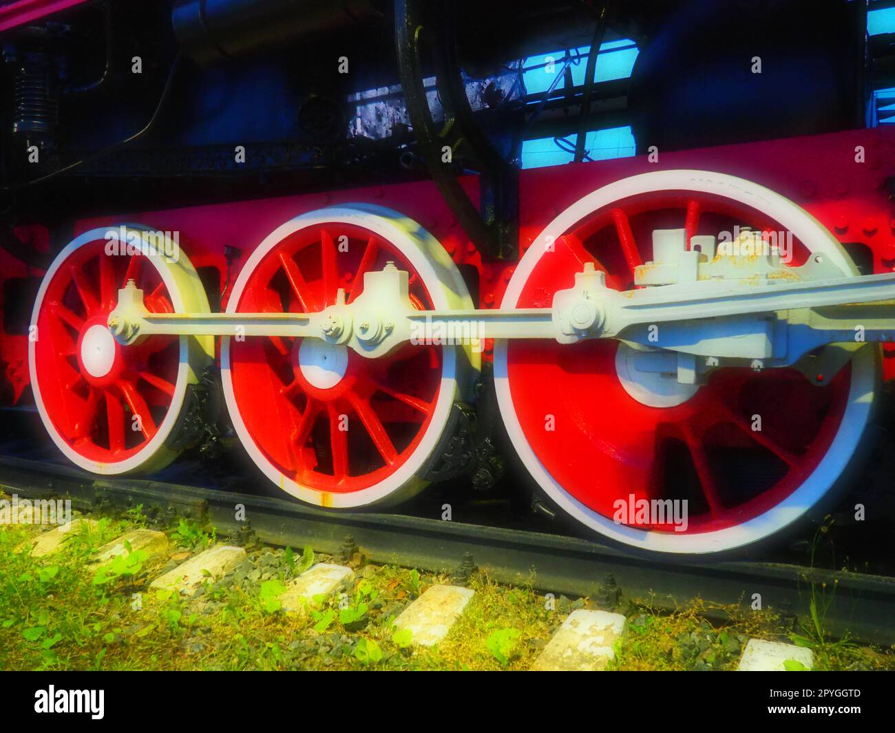 Ravvicinata delle ruote vintage di una locomotiva o di un treno. Ruote in metallo pesante grandi rosse con meccanismi di guida pistone. Locomotiva del XIX - XX secolo con motore a vapore. Foto brillanti e brillanti Foto Stock