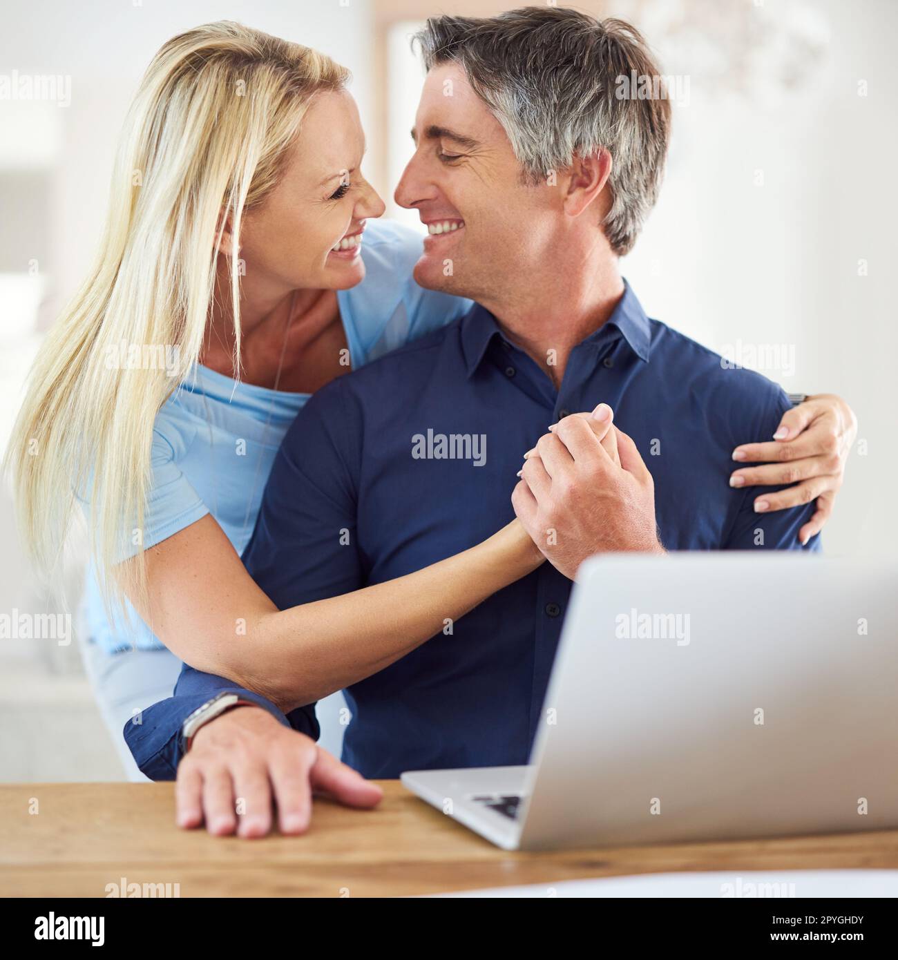 Insieme per sempre. una donna matura e attraente che abbraccia il suo bel marito maturo mentre usa un computer portatile in casa. Foto Stock