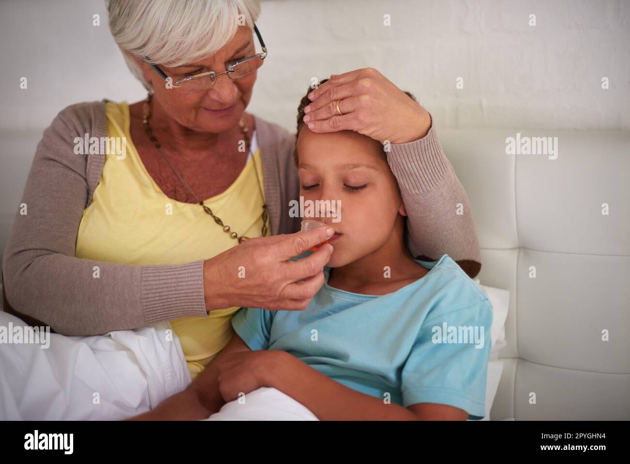 La medicina aiuterà con i sniffle. una nonna premurosa che si prende cura del suo nipote malato a casa. Foto Stock