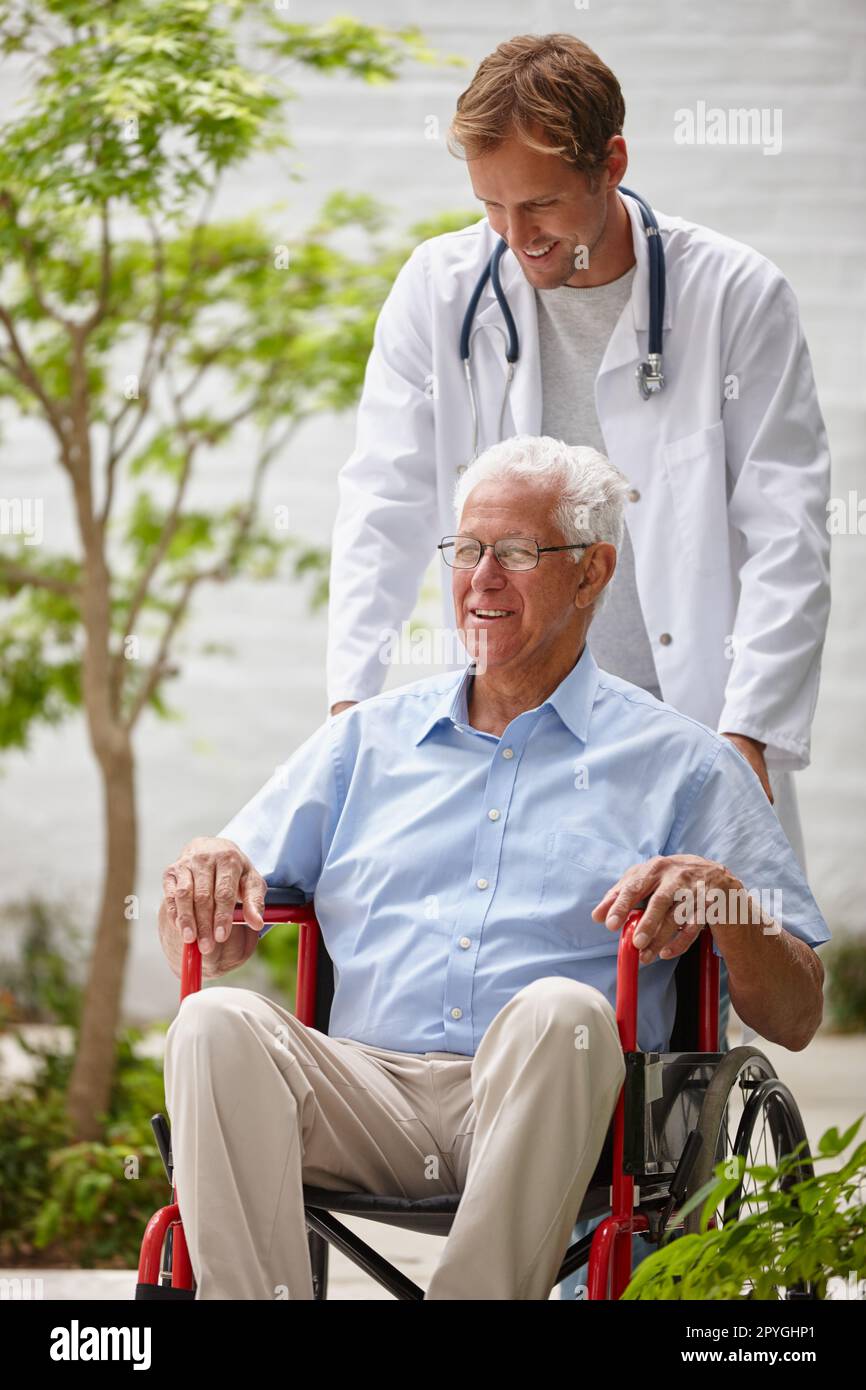 Prendersi cura del benessere generale dei suoi pazienti. un medico maschio che spinge il paziente anziano in una sedia a rotelle all'esterno. Foto Stock