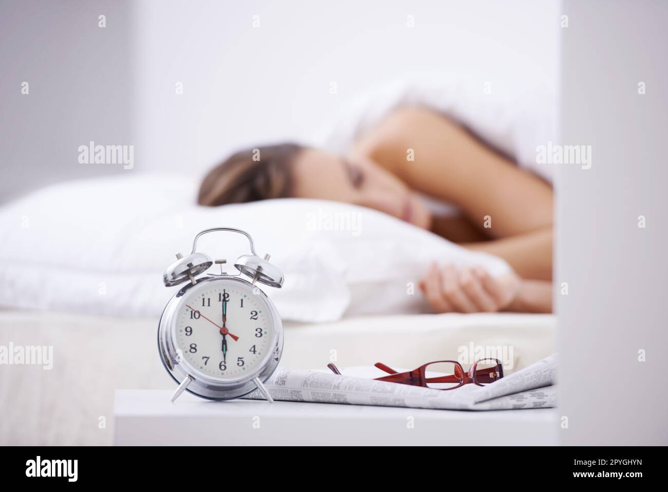 Ottenere il suo 8 ore. Una donna che dorme nel suo letto con una sveglia in primo piano. Foto Stock