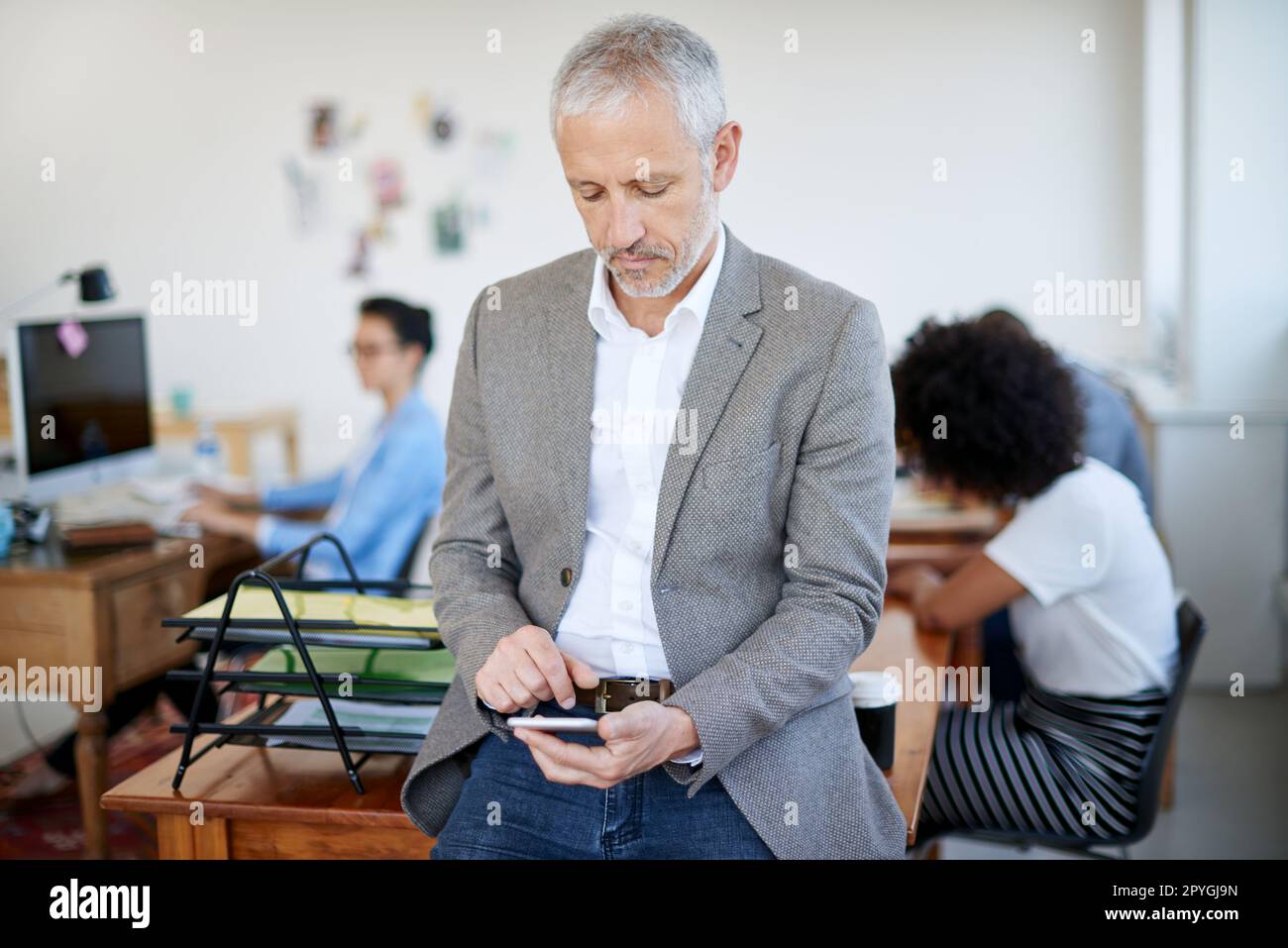 Invio di alcuni aggiornamenti client. un uomo d'affari maturo che usa un cellulare mentre si siede su un tavolo in un ufficio. Foto Stock