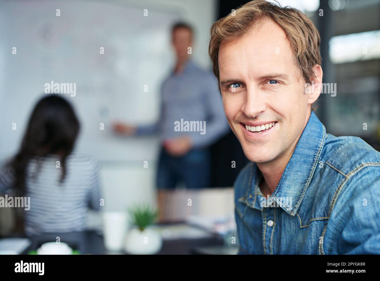 Il successo nasce tra queste quattro mura. Ritratto di un lavoratore in ufficio seduto in una riunione con i suoi colleghi sullo sfondo. Foto Stock