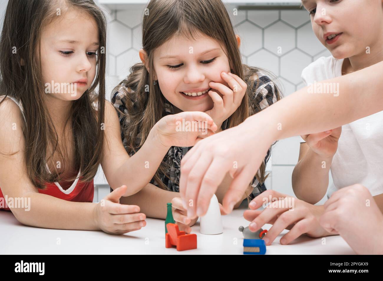 Bambini sorridenti e concentrati che giocano con i giocattoli dei mobili su un tavolo bianco. Immaginazione e giochi creativi per bambini Foto Stock