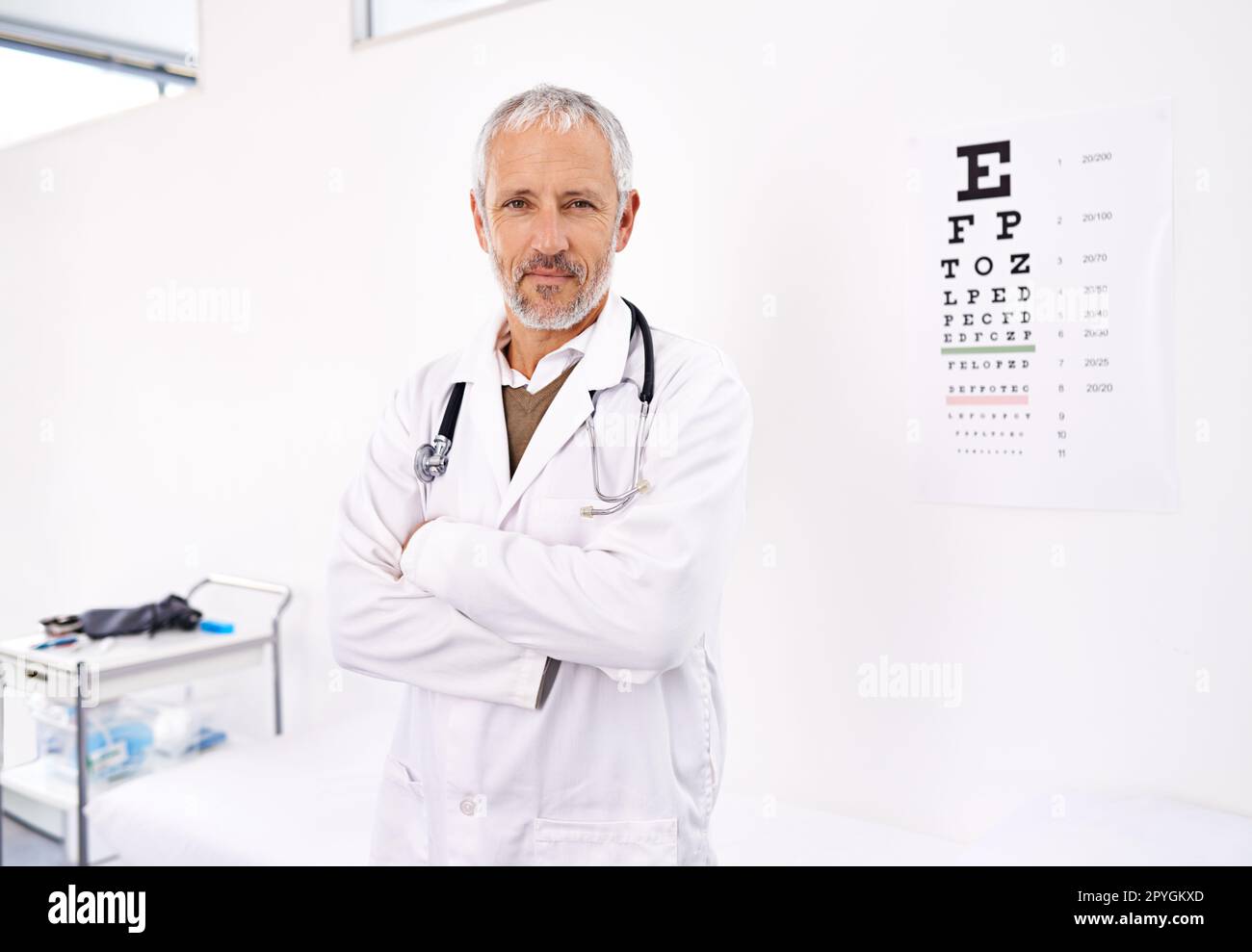 Potete leggere che cosa sul grafico lascia vedere. Ritratto di un optometro maschio maturo in piedi nel suo ufficio con una mappa degli occhi sullo sfondo. Foto Stock