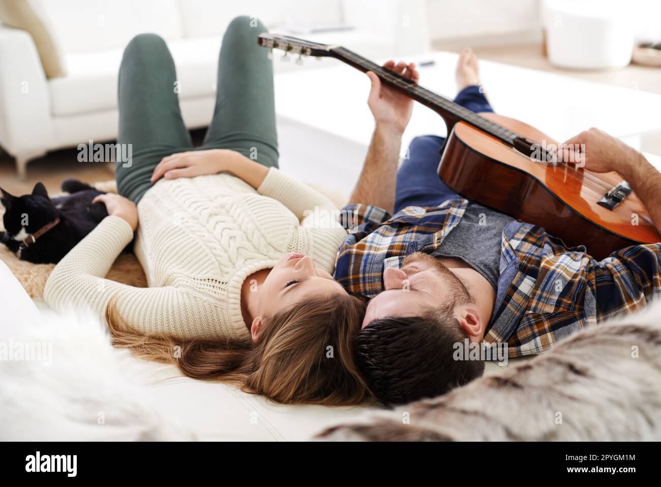 La sua canzone sull'amore e i gatti. un giovane che suona la chitarra mentre si sdraia sul pavimento con la sua ragazza. Foto Stock