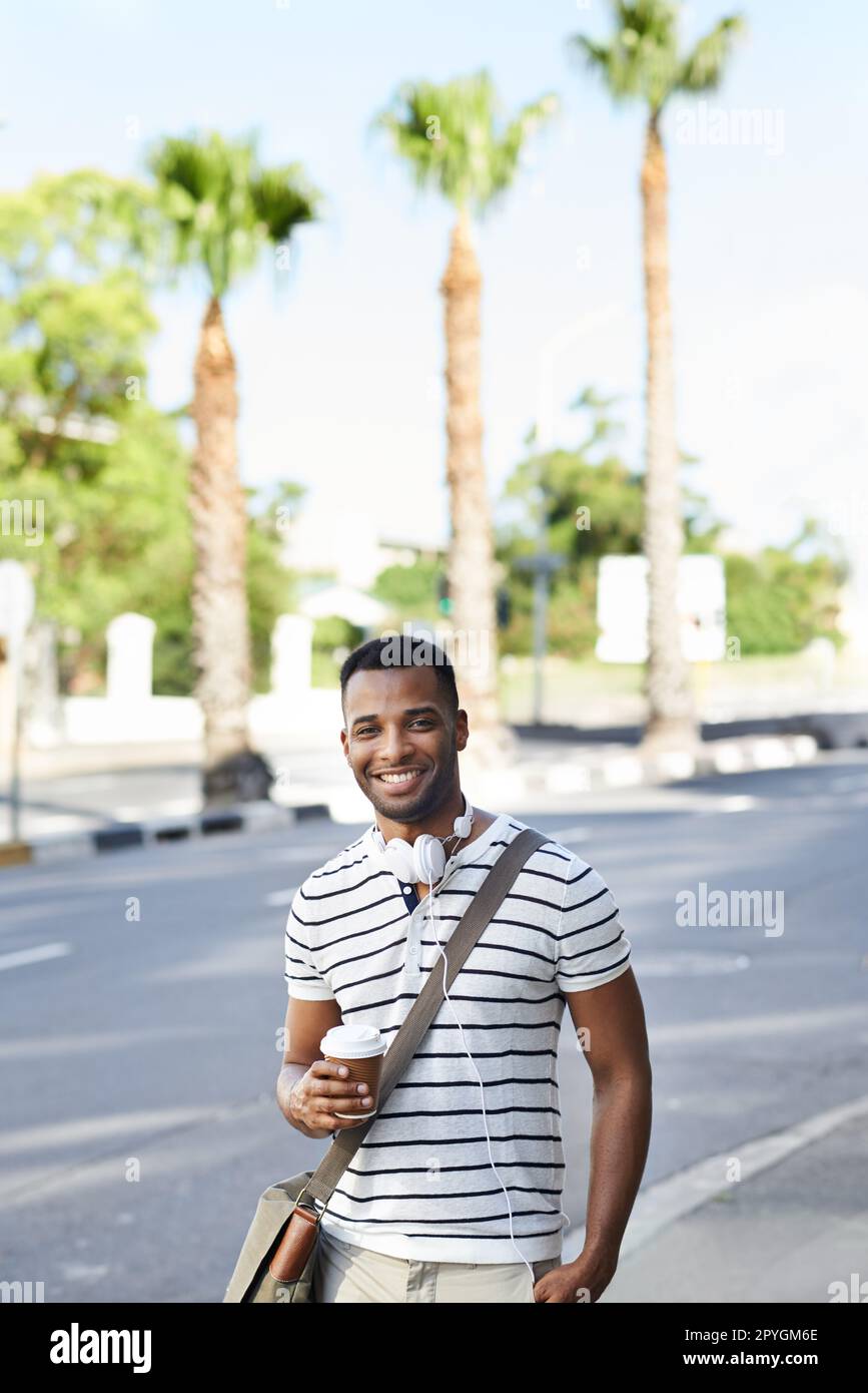 Passeggiando per la città. Un bell'uomo d'affari afro-americano vestito casualmente in città con le sue cuffie intorno al collo. Foto Stock
