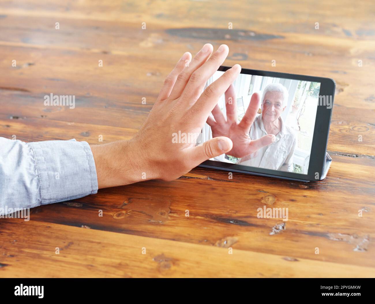 Raggiungere .... vista ritagliata di una mano di un giovane mans che sventolano verso la sua famiglia in una videochiamata. Foto Stock