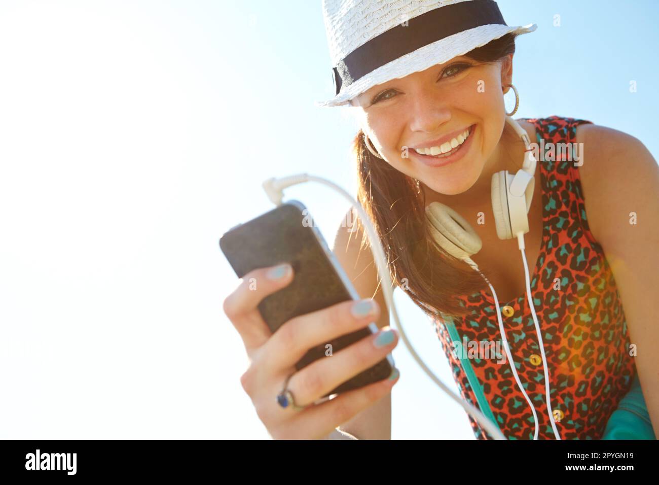 Qual è la tua canzone preferita. Una ragazza giovane felice sorridente mentre tiene uno smartphone con le cuffie collegate. Foto Stock