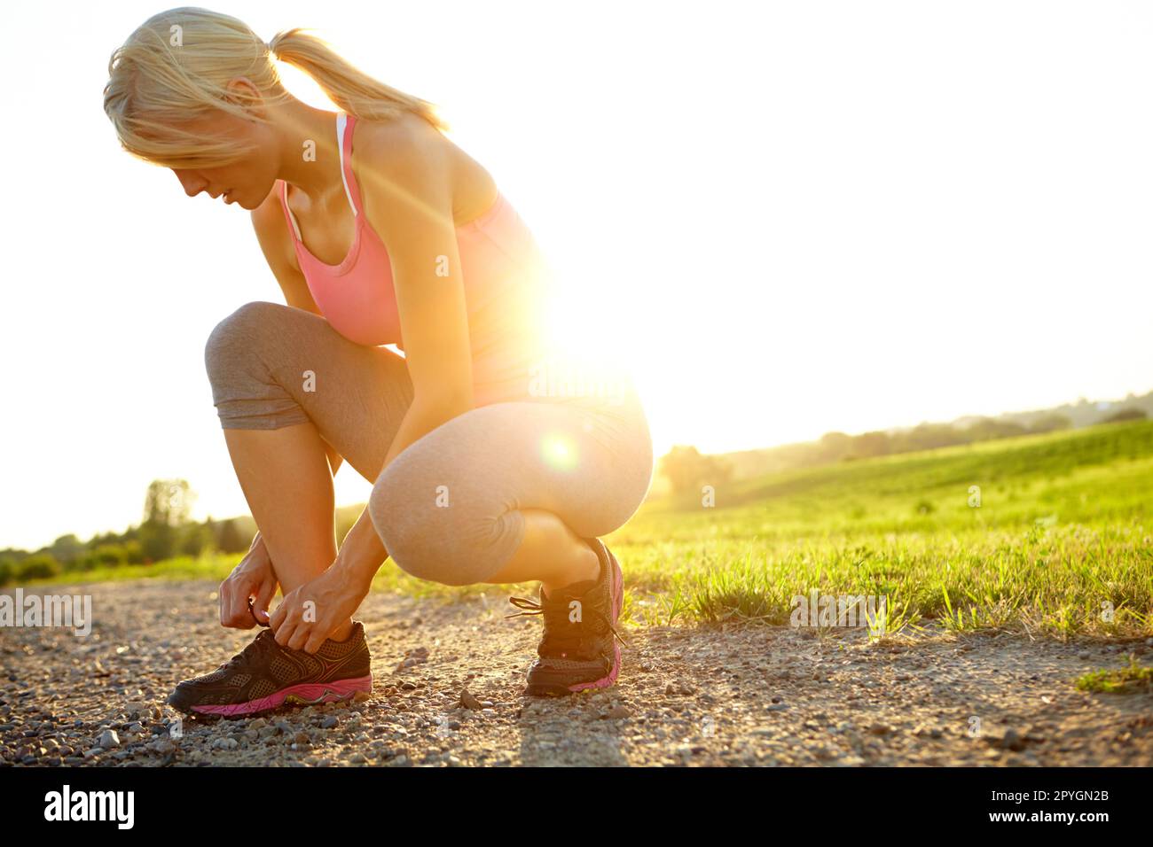Indossare le scarpe da running. Una giovane donna in abbigliamento sportivo che le lega le scarpe. Foto Stock