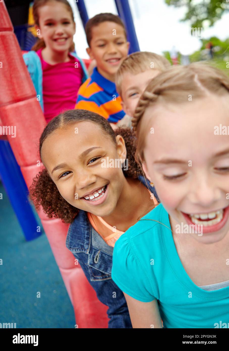 L'infanzia sorride e divertimento. Un felice gruppo di bambini multietnici seduti felicemente su uno scivolo in un parco giochi. Foto Stock