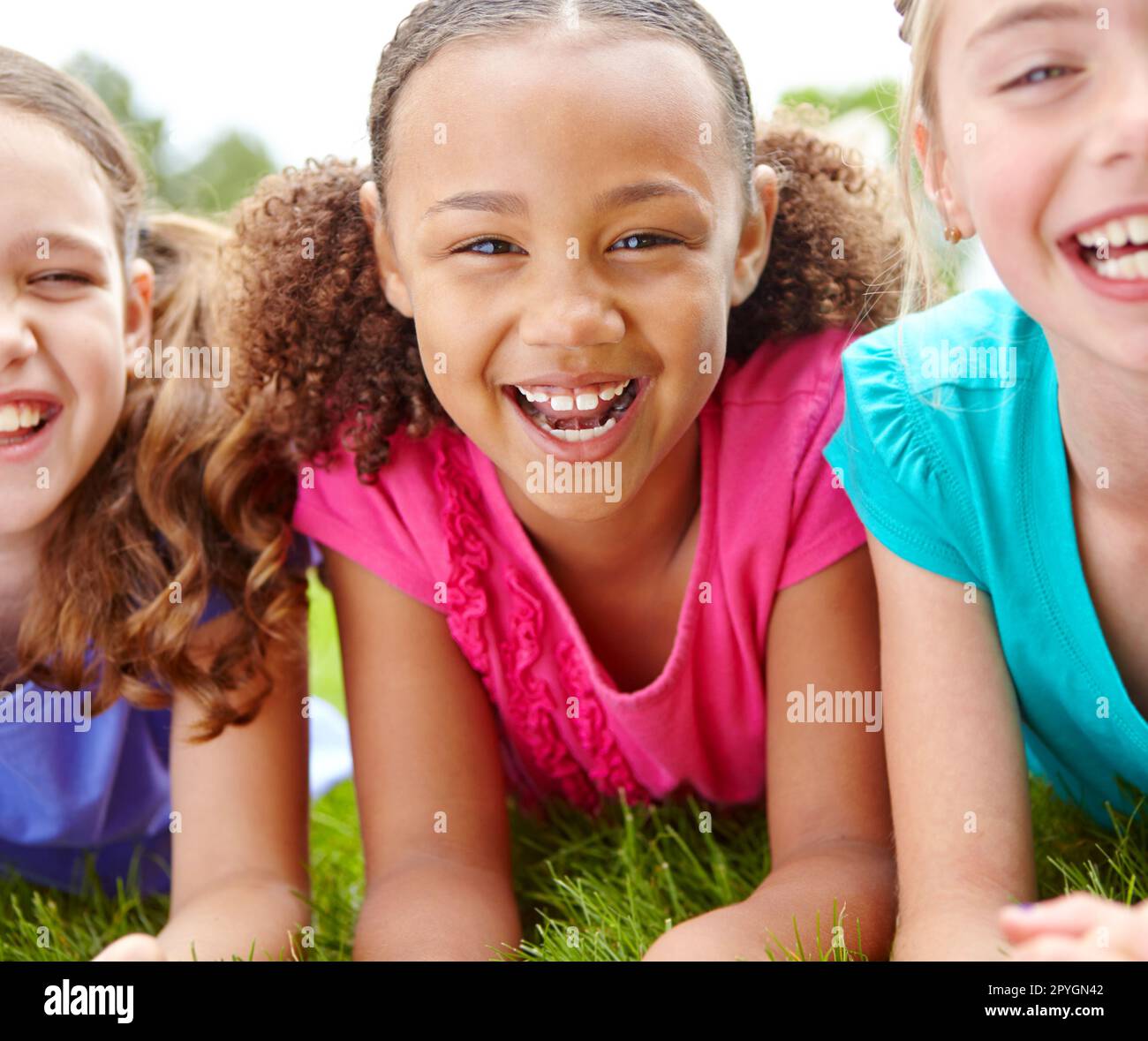 Si diverte sempre con i suoi migliori amici. Tre ragazze multietniche sdraiate sull'erba in un parco sorridendo alla macchina fotografica. Foto Stock