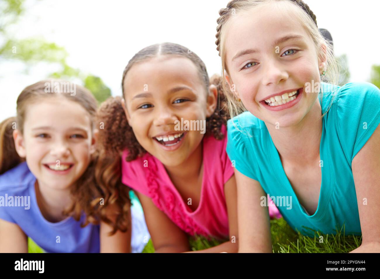 Divertirsi insieme. Tre ragazze multietniche sdraiate sull'erba in un parco sorridendo alla macchina fotografica. Foto Stock