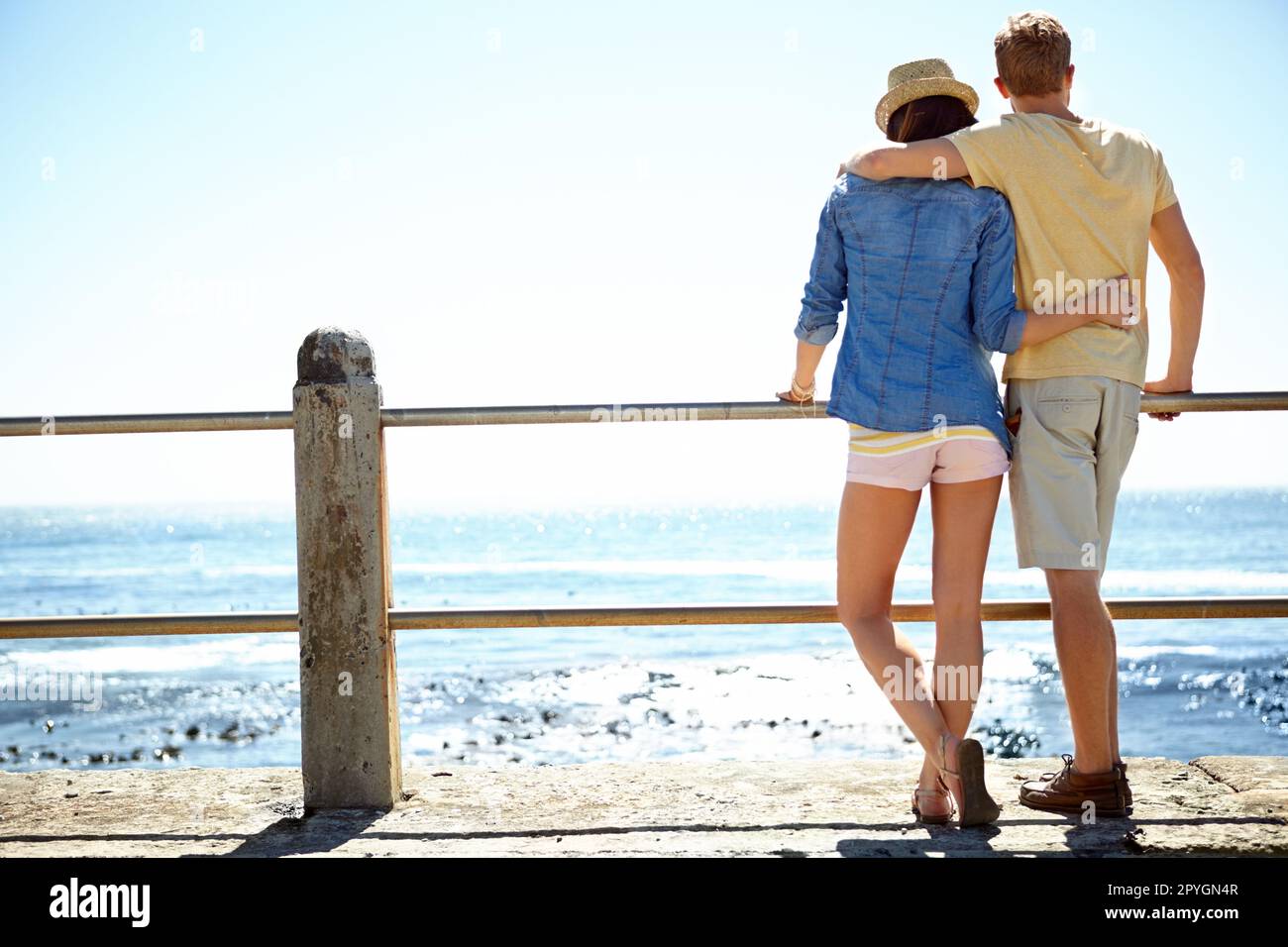 Apprezzare la vista. Vista posteriore di una giovane coppia in piedi su un molo che guarda all'oceano. Foto Stock