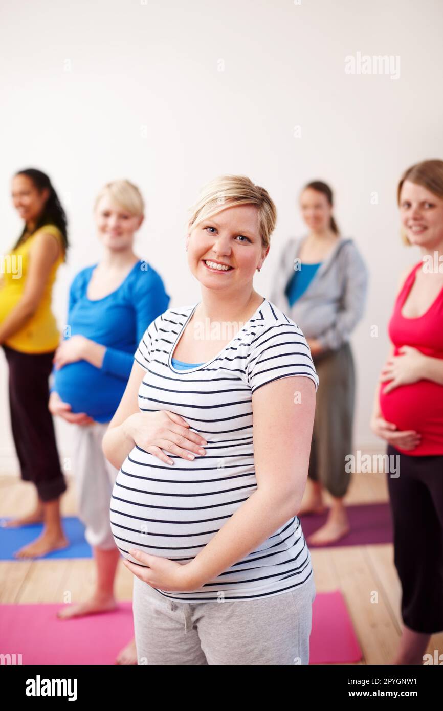 Ottenere il massimo dalla maternità. Un gruppo multietnico di donne incinte in piedi in una classe di esercizio sorridendo felicemente alla macchina fotografica. Foto Stock