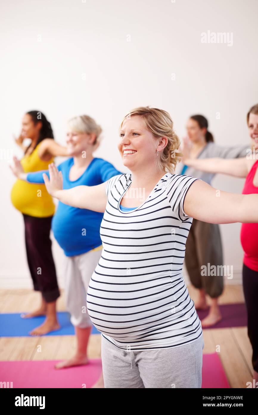 Preparare i nostri corpi alle sfide della maternità. Un gruppo multietnico di donne incinte che fanno esercizi con le braccia tese al lato. Foto Stock