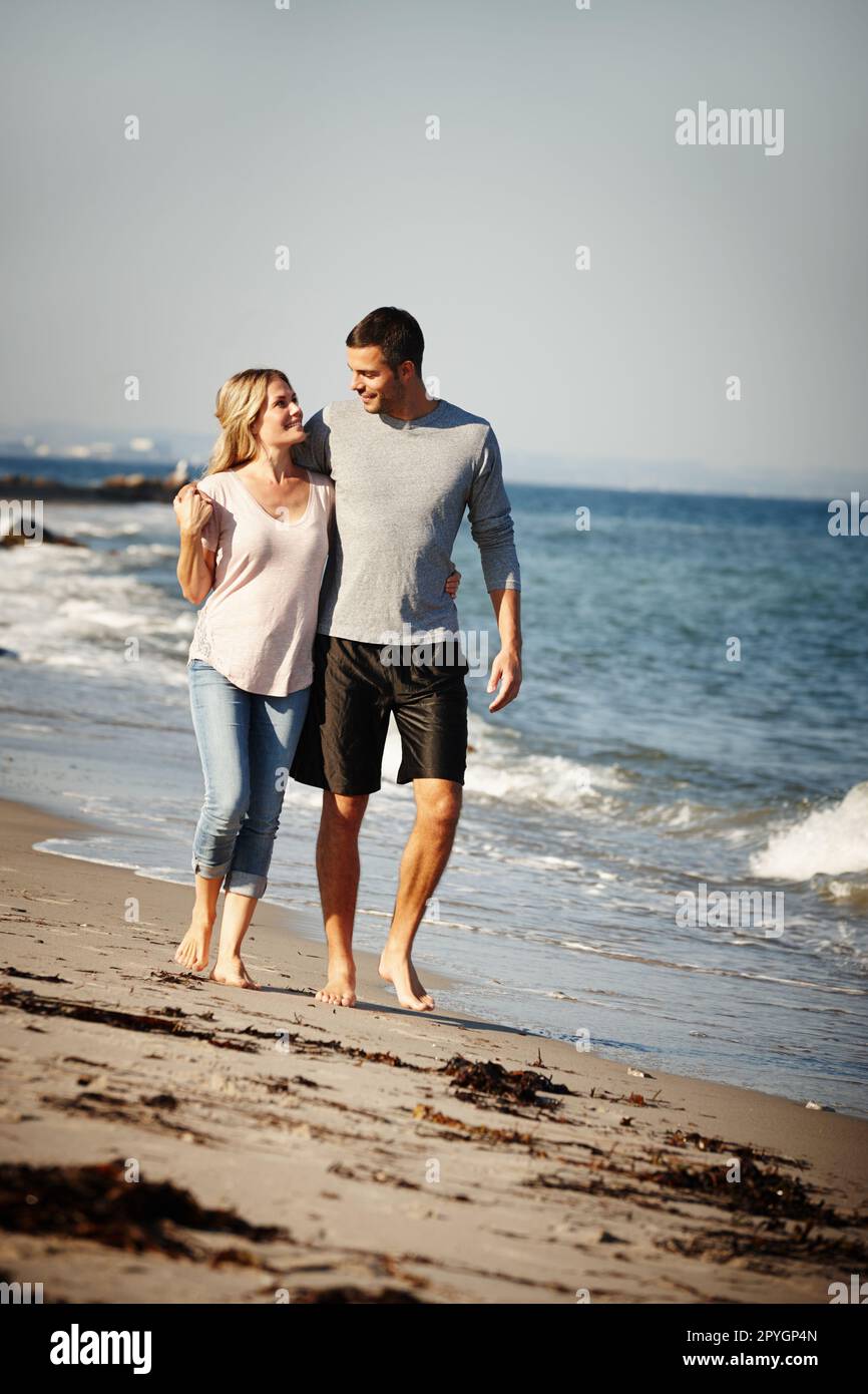 Abbiamo tutta la spiaggia a noi stessi. Foto a tutta lunghezza di una giovane coppia con braccio a piedi lungo una spiaggia sabbiosa. Foto Stock