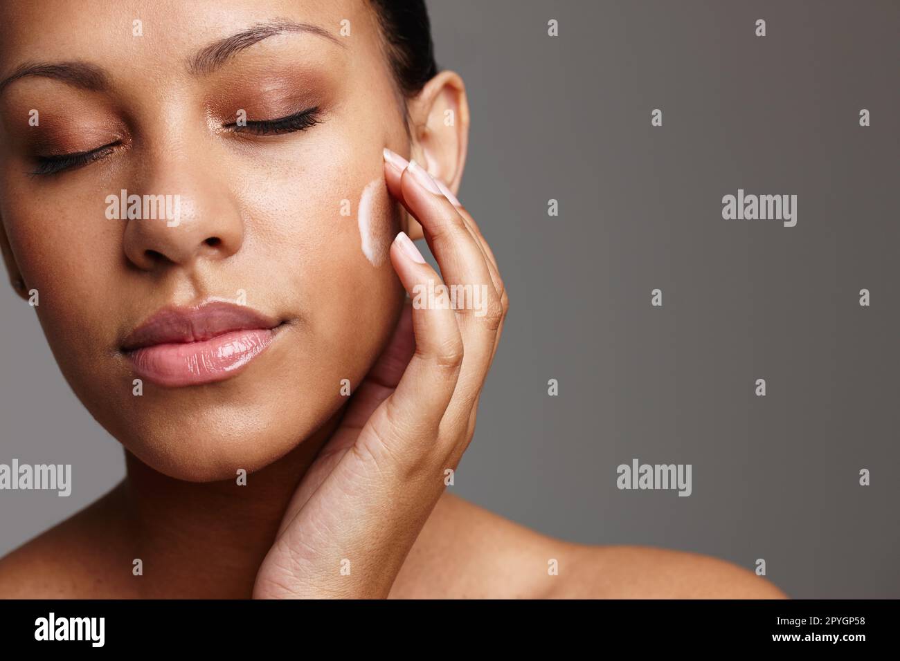 Le più eque di tutte. una bella giovane donna che applica la crema per il viso mentre si trova in uno studio. Foto Stock