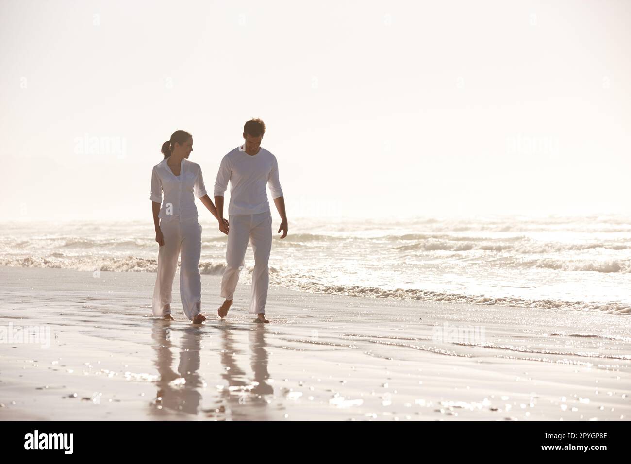Passeggiando lungo la spiaggia con qualcuno di speciale. Foto a tutta lunghezza di una giovane coppia vestita di bianco che cammina lungo una spiaggia. Foto Stock