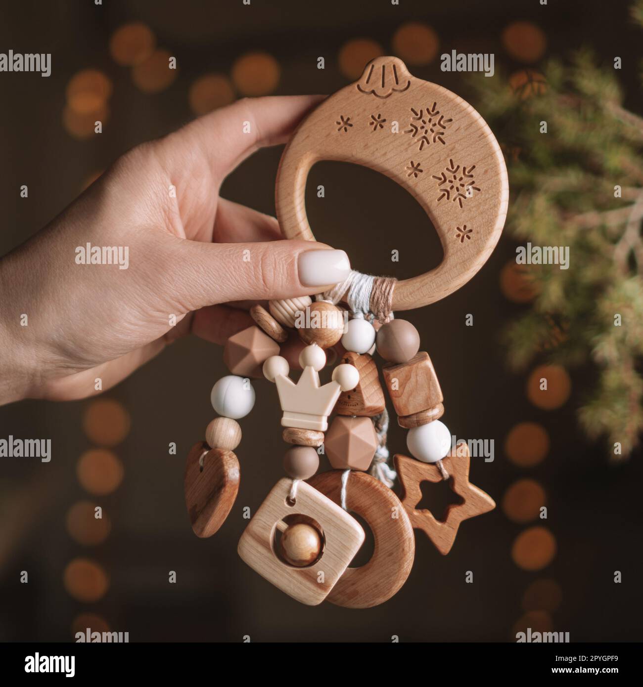 Massaggiagengive per bambini a forma di palla natalizia in legno con perline in silicone in mano alla donna, sfondo scuro con luci a ghirlanda Foto Stock