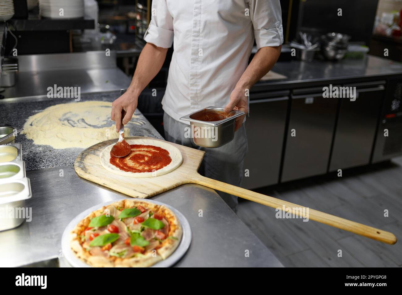 Chef maschile spalmare pasta di pomodoro su base pizza Foto Stock