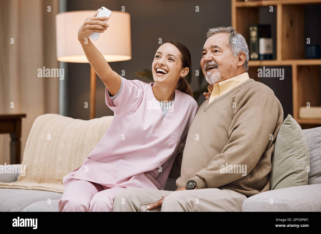 Infermiere, selfie e anziano in casa di cura con smartphone e sorriso per foto, assistenti e pensionati. Salute, fotografia con telefono e assistenza, giovane donna e infermieristica con uomo anziano benessere. Foto Stock